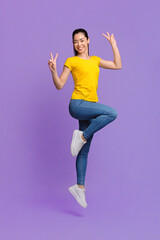 Carefree Mood. Cheerful Asian Girl Jumping In Air And Showing Peace Gesture