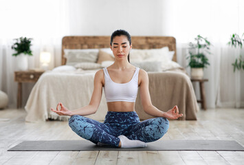 Asian Woman Meditating At Home, Sitting In Lotus Position In Living Room