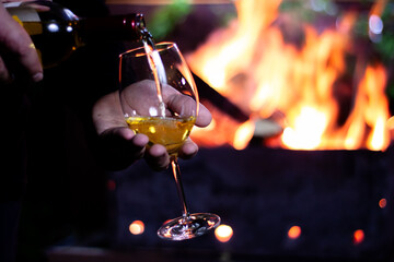 Obraz na płótnie Canvas pour a glass of white wine from a bottle on the background of a barbecue with fire