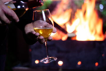 Fototapeta na wymiar pour a glass of white wine from a bottle on the background of a barbecue with fire