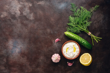 Fototapeta na wymiar Traditional greek tzatziki sauce with ingredients on dark rustic background. Greek yogurt with cucumber, dill, garlic and lemon. Top view, copy space, flat lay.