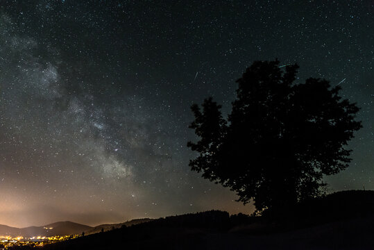 Sternenhimmel mit der Milchstra&szlig;en Galaxie im Sommer mit einem Baum vor einer beleuchteten Stadt,  Deutschland