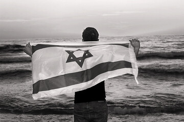 Israeli patriot with the flag of Israel stands on the shores of the Sea at sunset. Independence day...