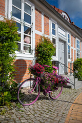 in front of old half-timbered house stands a bicycle planted with flowers for decoration