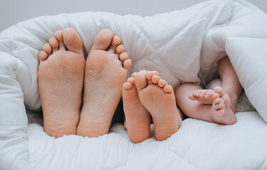 Close-up of the legs of the family of mom, daughter and little newborn son, covered with a plaid. Sleeping family. Time to sleep. Photography, concept.