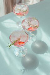 Glasses of strawberry cocktail or mocktail, refreshing summer drink with crushed ice and sparkling water on light blue background.