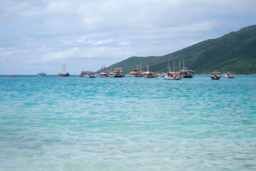Several tourist boats in clear azure water of an ocean against a background of green mountains.