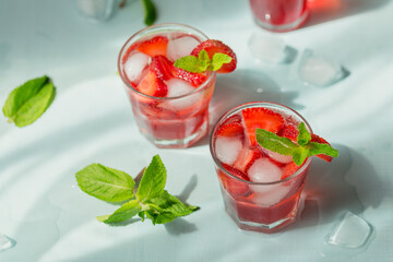 Summer drink with sparkling wine. Homemade refreshing fruit cocktail or punch with champagne, strawberries, ice cubes and rosemary on light blue background.