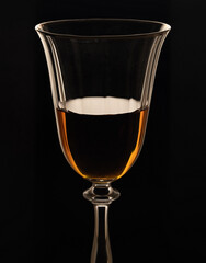Wine glass with cognac. Fjer with amber cognac on a black background.