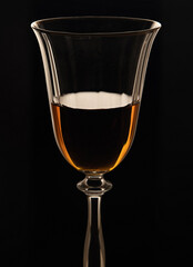 Wine glass with cognac. Fjer with amber cognac on a black background.