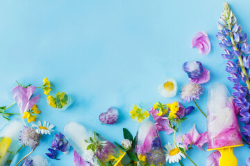 Floral Ice Pops. Colorful wildflowers in frozen popsicles and ice cubes on blue background flat lay and fresh summer flowers. Copy space. Hello summer concept. Creative bright image