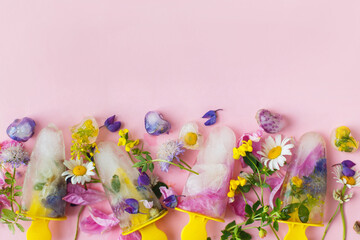 Floral Ice Pops. Colorful wildflowers in frozen popsicles and ice cubes on pink background flat lay and fresh summer flowers. Copy space. Hello summer concept. Creative bright image