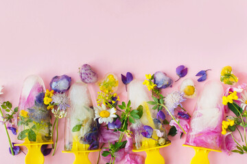 Floral Ice Pops flat lay. Colorful wildflowers in frozen popsicles and ice cubes and fresh summer flowers on pink background. Copy space. Hello summer concept. Creative bright image