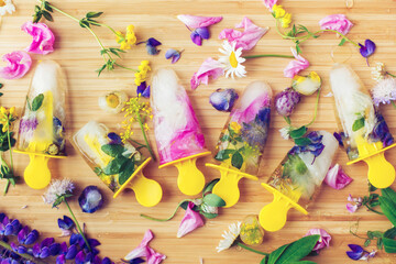 Floral Ice Pops flat lay. Colorful wildflowers in frozen popsicles and ice cubes and fresh summer flowers on wooden background.  Creative image. Hello summer concept.