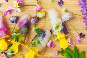 Hello summer concept. Floral Ice Pops flat lay. Colorful wildflowers in frozen popsicles and ice cubes and fresh summer flowers on wooden background.  Creative image