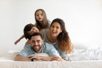 Happy young parents with little children lying on bed looking at camera. Smiling beautiful mother and bearded father enjoying free time with cute adorable daughter and son.