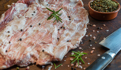 Close up of raw pork Secreto de ventresca pure iberico, iberian pig cut, with himalayan pink salt, pepper in grains, rosemary and a knife on a wooden board