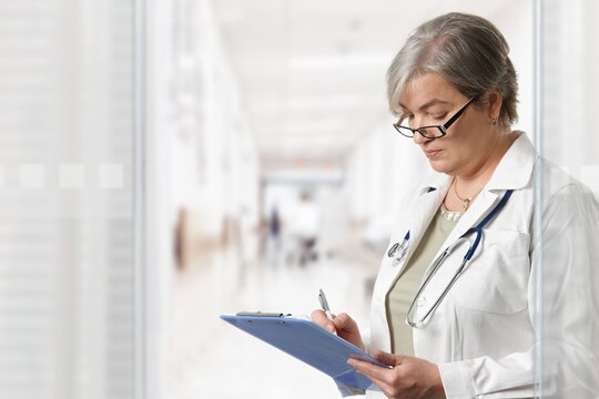 Mature female doctor standing on hospital corridor, looking at clipboard. 