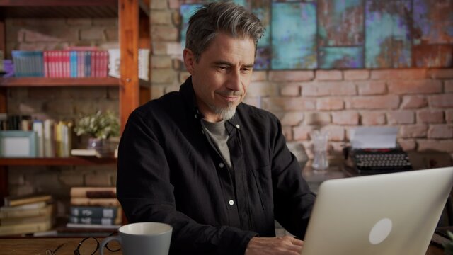 Portrait of happy mature man sitting at table using laptop at home working in home office. 