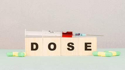 wooden cubes with word dose pills and syringe on green table