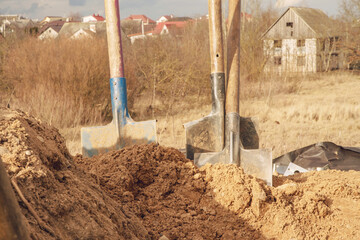 Fototapeta na wymiar shovels with old wooden handles stuck in ground against village under cloudy sky