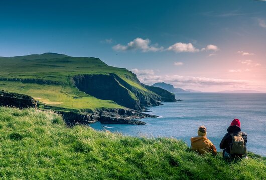 A woman and girl are sitting at the high cliff and looking at the sea.