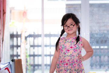 Asian child girl of Thai-Chinese descent stands sweet smile for photographer. She wears glasses for...
