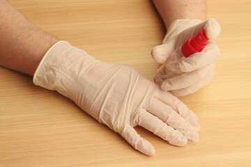 Doctor’s hands in white medical gloves on the table with antibacterial antiseptic. Sanitizer for...
