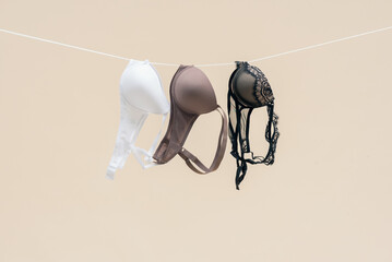Female bra is hanging on the rope isolated on a light background. - obrazy, fototapety, plakaty