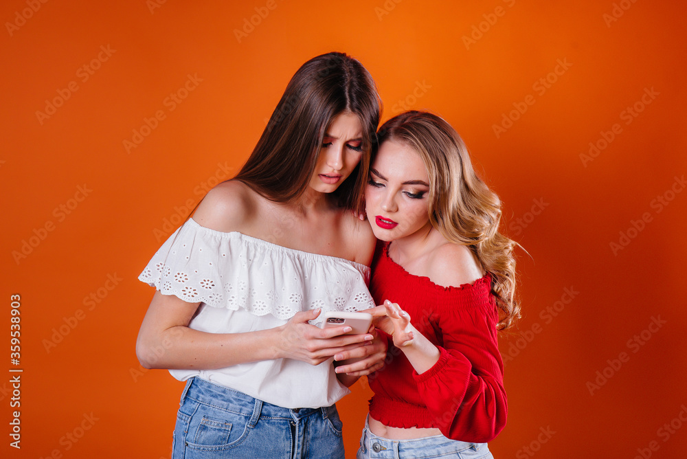 Wall mural two young and beautiful girls take a selfie and watch the phone in the studio on a purple background