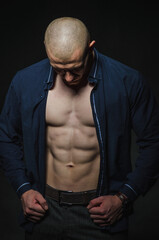 Fototapeta na wymiar A stylish, bald young man stands with a naked torso on a dark background in the category