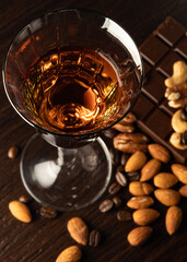 Cognac wine glass with amber cognac, nuts lying near the wine glass, coffe grains, chocolate bar on...