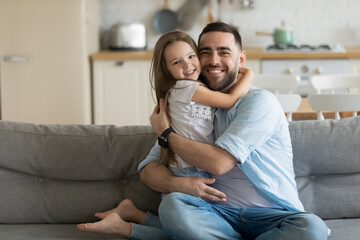 Close up headshot portrait picture of smiling father hugging daughter sitting on coach couch at...
