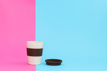 A cup of natural bamboo on a pink-blue background. Brown cap, a cup for hot coffee and tea.