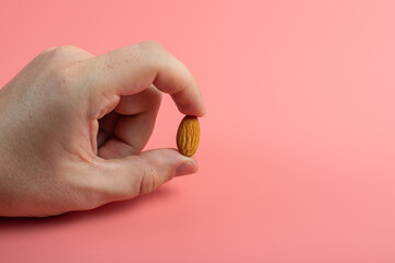 Fototapeta na wymiar fingers holding almond single almond seed on pink background