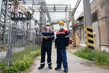 Engineers electrical substations conduct a survey of modern high-voltage equipment in the mask at the time of pandemia. Energy. Industry