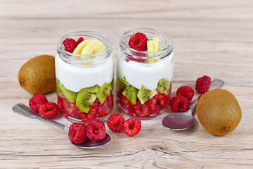Two glasses of healthy layered snack with raw raspberry and kiwi fruits and yoghurt surrounded by ingredients
