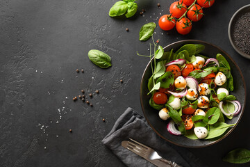 Homemade salad with spinach, cherry tomatoes, basil, onion and Mozzarella. Vegan food. Tasty and healthy meal on black stone background. Top view. Copy space.
