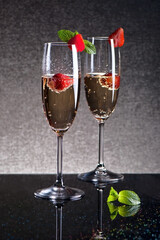 Two glasses of champagne with strawberries on a black table, shot in low key