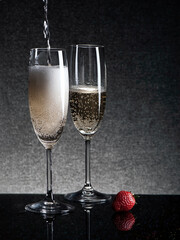 Two glasses of champagne with strawberries on a black table, shot in low key