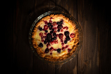 Baked round homemade cheesecake with berries. Pie on an old dark wood table. Flatlay background.