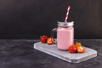 Refreshing summer pink drink with strawberries on a dark, worn surface