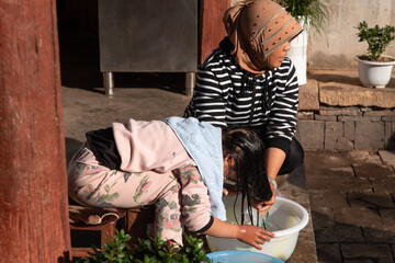  February 2019. Woman washes her daughter's hair. daily life scene in rural village in Yunnan,...