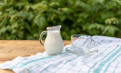 on a wooden table with a white tablecloth is a glass jug of milk 