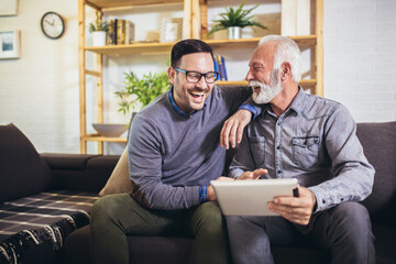 Portrait of senior man with adult son using digital tablet at home
