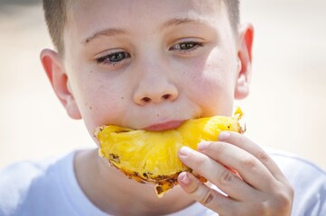 Cute Caucasian baby boy eating fresh pineapple outside in the summer heat.