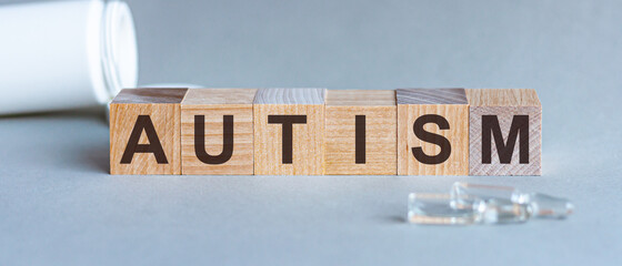Word AUTISM. Autism text on wooden blocks. In front of a row of cubes are ampoules, in the background - white plastic packaging from tablets, the cubes are located on a gray surface. Concept Image.