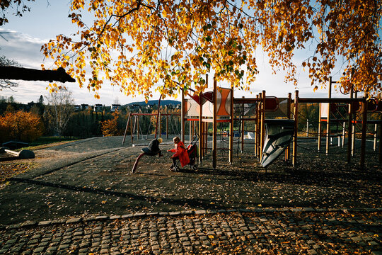 A borther and sister playing at the playground having so much fun. Natural light in this beautiful evening in the autumn. Leaves are everywhere.