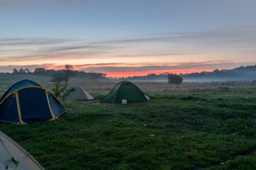 Tourist tents in the field. Tourist camp in the fog. Morning fog at sunrise.