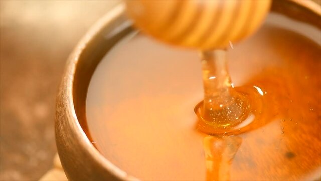 Honey dripping, pouring from honey dipper in wooden bowl.  Close-up. Healthy organic Thick honey dipping from the wooden honey spoon, closeup. 4K UHD video footage. Slow motion